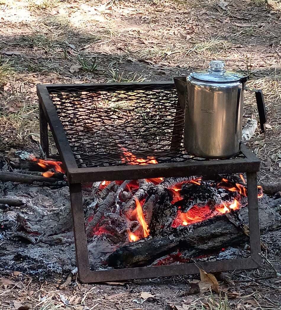 A percolator on a grate over the coals of a wood fire